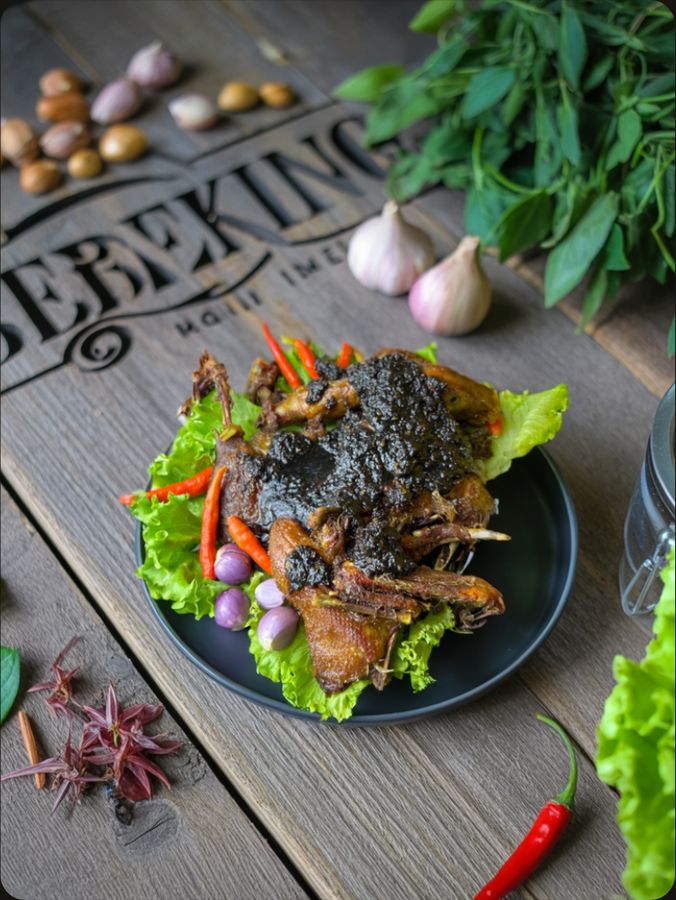 Bebek bumbu hitam pekat di atas daun selada dengan bawang merah