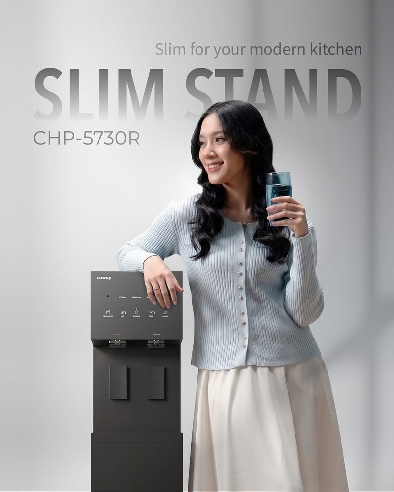 Wanita tersenyum memegang gelas air bersandar pada Coway Slim Stand CHP-5730R hitam berdesain ramping, pilihan water purifier modern yang bisa dipesan melalui Jamie Waterman